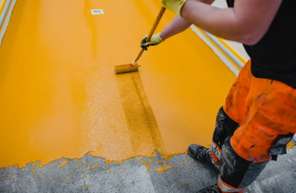 Worker painting yellow floor with roller.