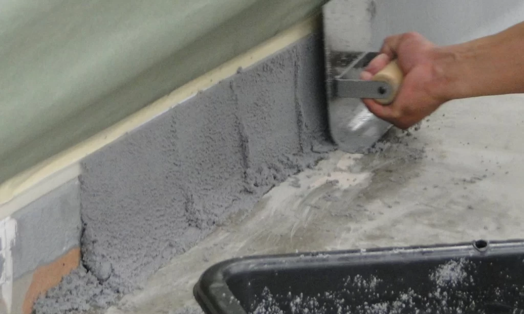 A person is using a paint roller to fill the gap between two walls.